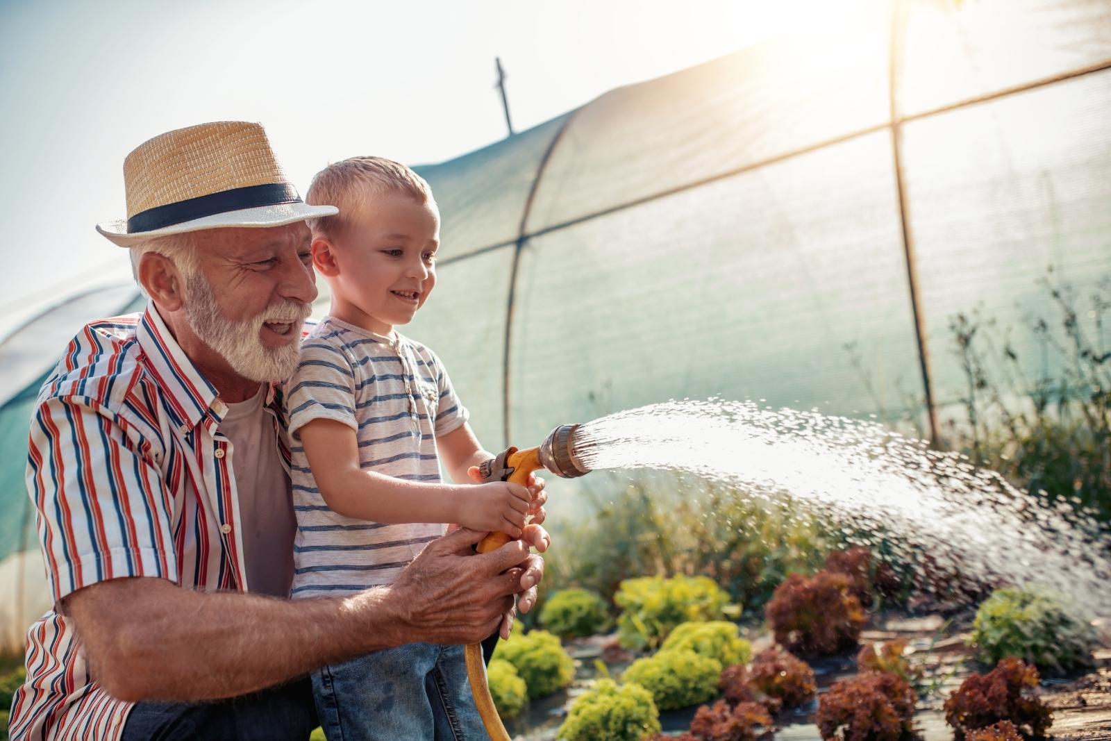 Elderly man watering the ground with young boy